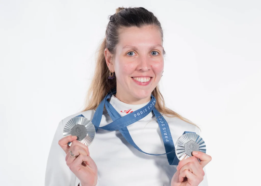Portrait d'Auriane Mallo souriante, ses deux médailles de Paris 2024 entre les mains, sur fond blanc