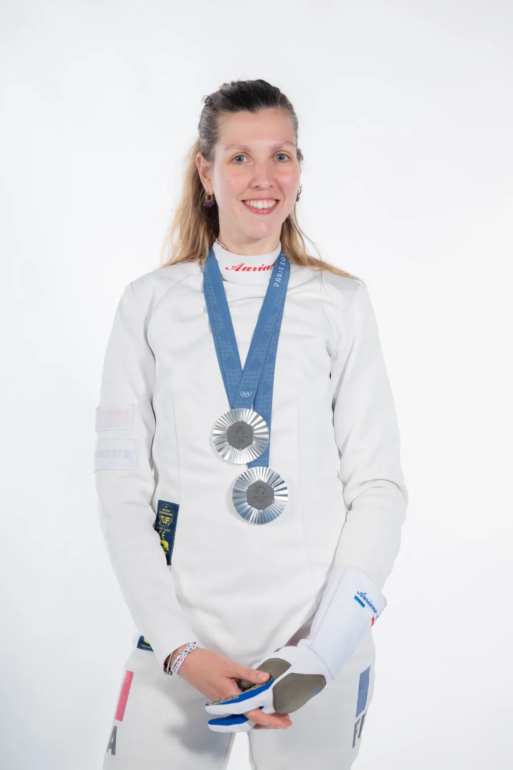 Portrait d'Auriane Mallo en tenue d'escrime avec ses médailles autour du cou, sur fond blanc
