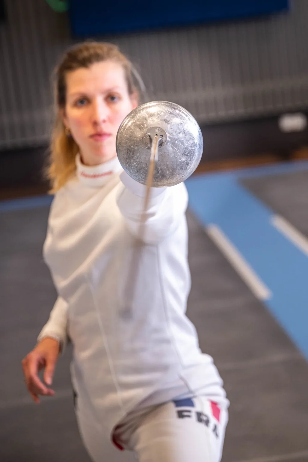 Auriane Mallo tendant son épée vers l'objectif dans la salle d'armes