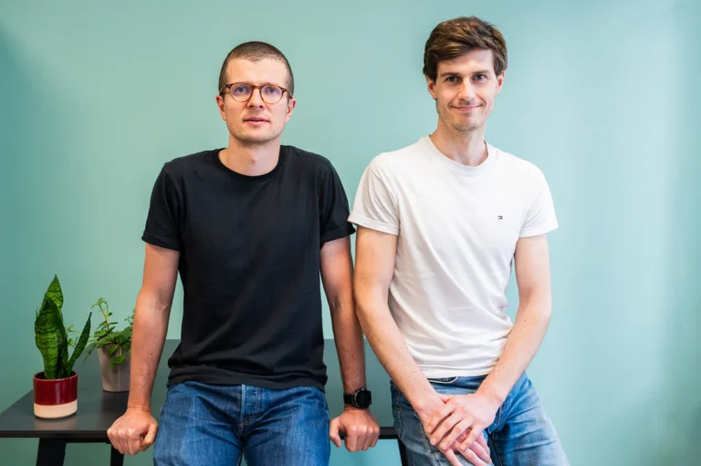 Portrait de deux membres de l'équipe FYGR posant côte à côte devant un mur turquoise