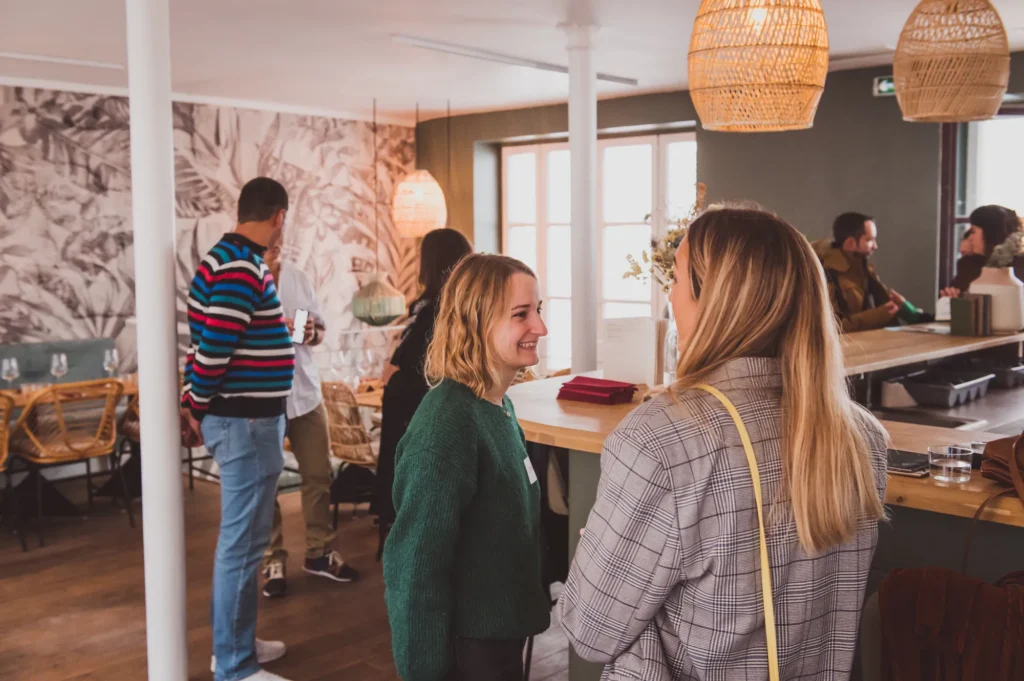 Invités qui discutent debout devant un papier peint tropical lors du déjeuner HomeExchange
