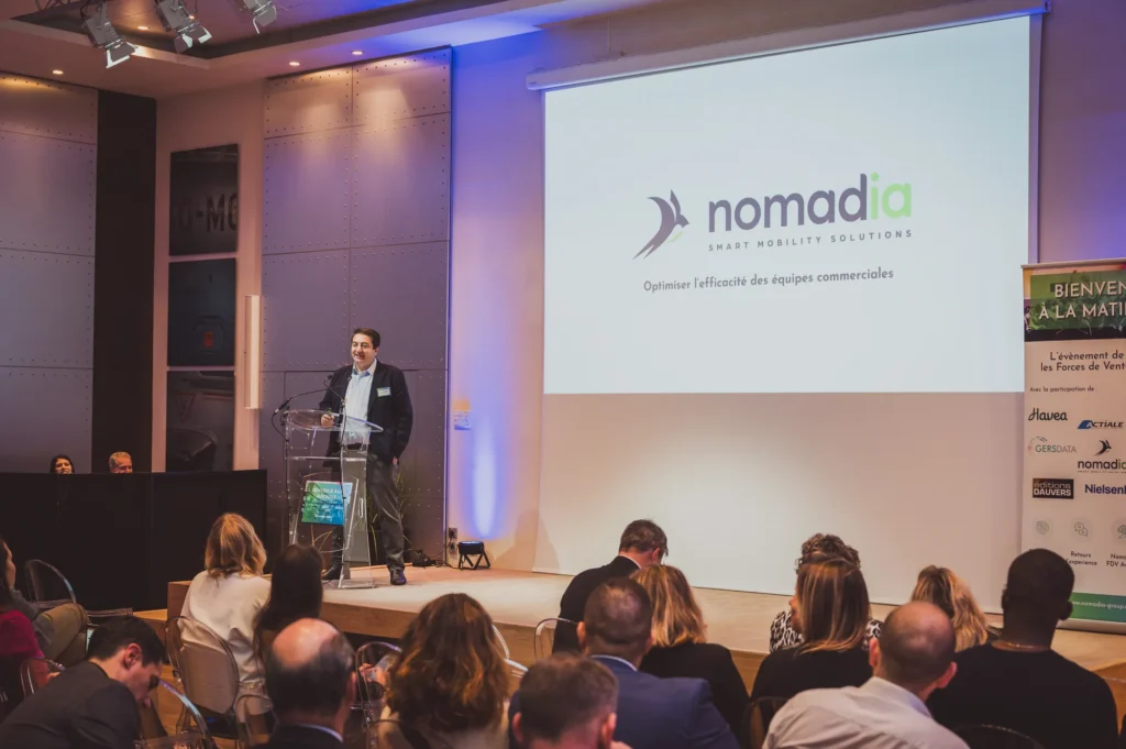 Écran de conférence affichant le logo Nomadia devant le public
