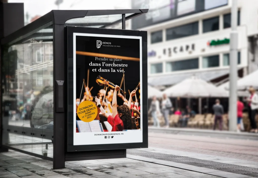Mockup d'une affiche d'abribus de la campagne « Donnons pour Démos » de la Philharmonie de Paris : « Prendre sa place dans l'orchestre et dans la vie »