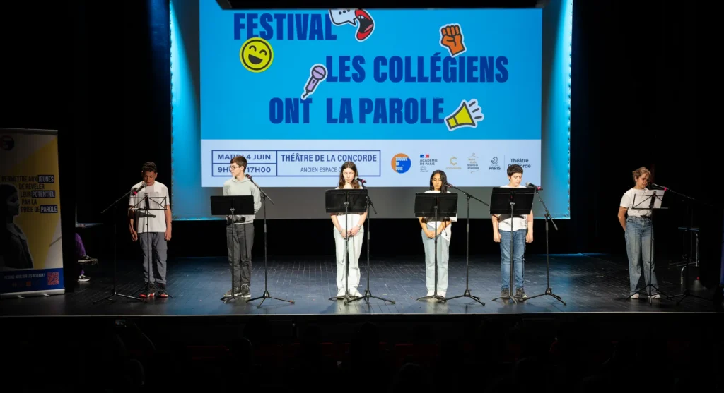 Élèves debout derrière des micros sur la scène, devant l'écran du festival