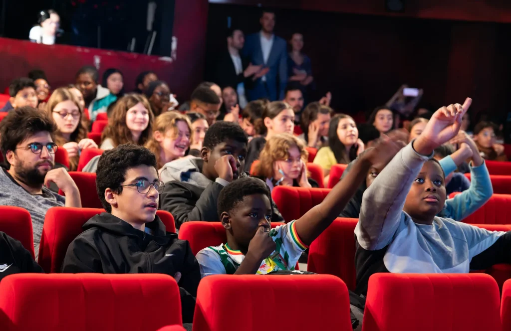 Collégiens dans la salle, bras levés, lors du festival Les collégiens ont la parole