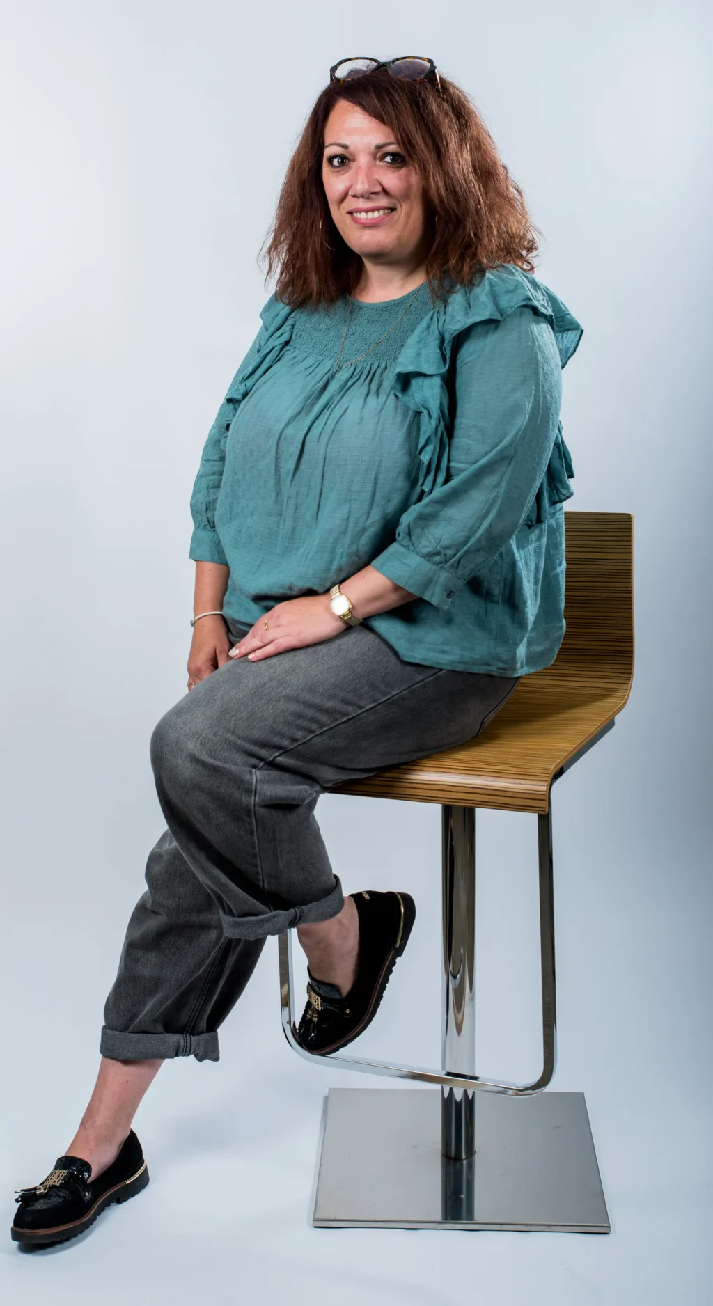 Portrait corporate d'un membre de l'équipe Yabuko en chemisier vert, assis sur un tabouret, sur fond clair