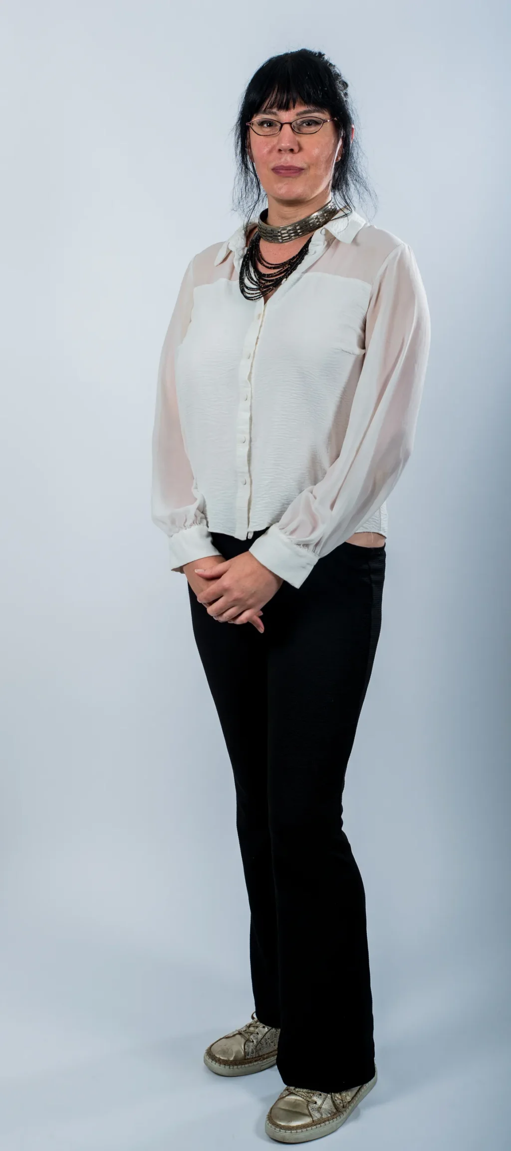 Portrait corporate en pied d'un membre de l'équipe Yabuko en chemisier blanc et pantalon noir, debout sur fond clair
