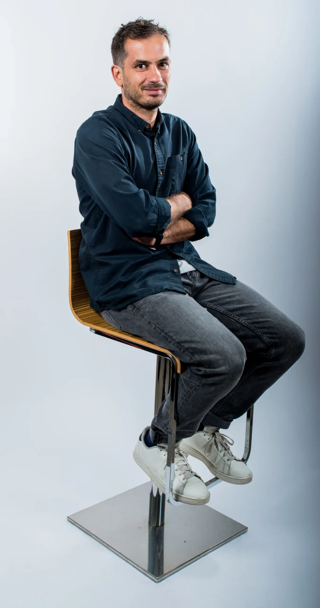 Portrait corporate d'un membre de l'équipe Yabuko en chemise sombre, assis sur un tabouret, bras croisés