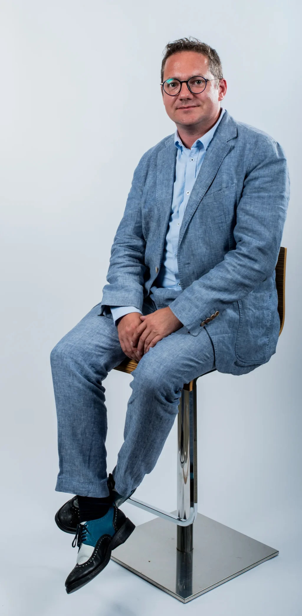 Portrait corporate d'un membre de l'équipe Yabuko en blazer bleu clair, assis sur un tabouret, sur fond clair